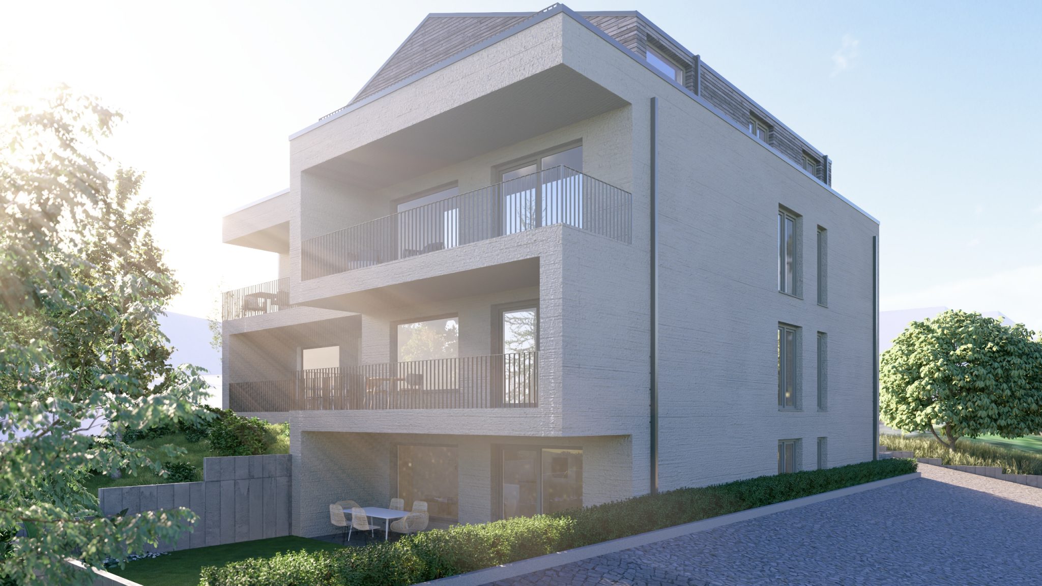 Mehrfamilienhaus mit übereinanderliegenden Balkonen in der Sonne, seitliche Ansicht mit Garten und gepflasterter Zufahrt.
