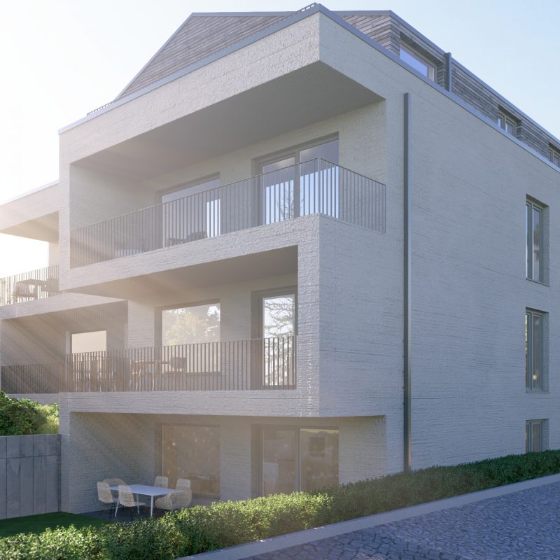 Mehrfamilienhaus mit übereinanderliegenden Balkonen in der Sonne, seitliche Ansicht mit Garten und gepflasterter Zufahrt.