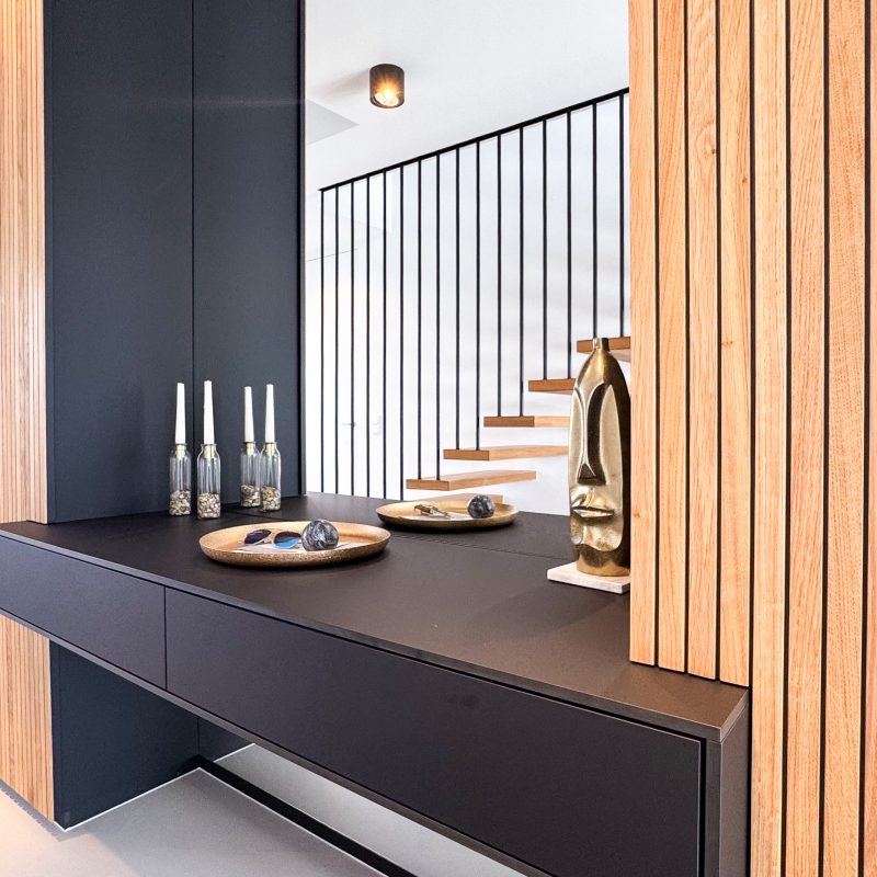 Detailansicht einer maßgefertigten Garderobenlösung mit Holzlamellenfront, schwarzem Sideboard und integriertem Spiegel.