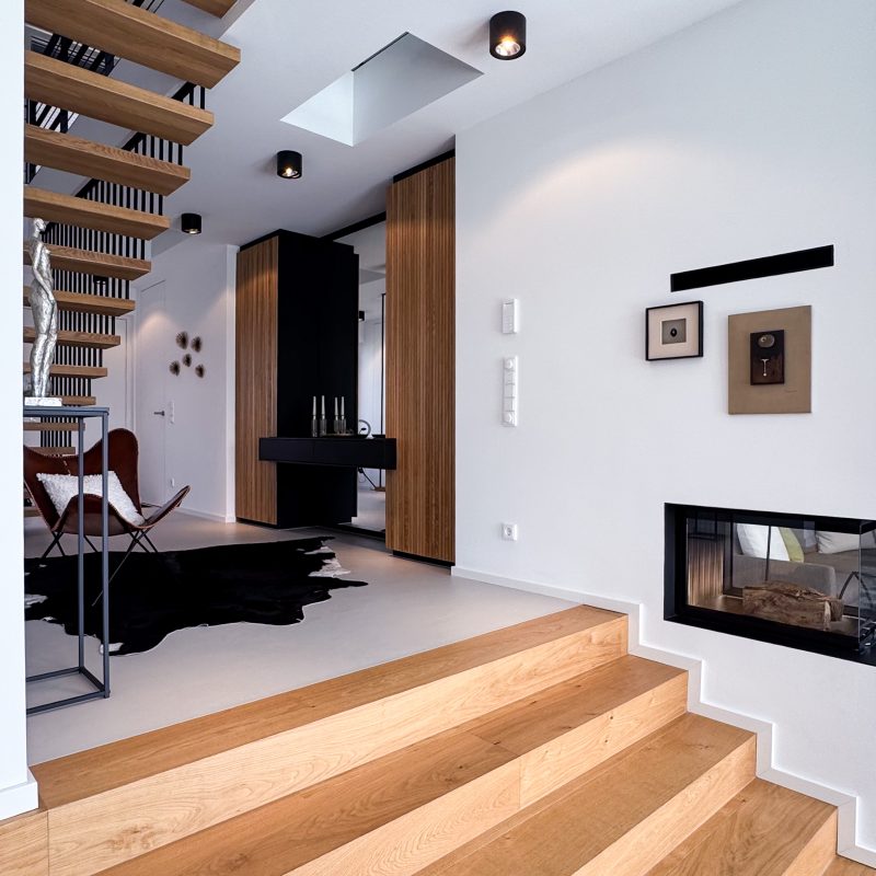 Moderner Eingangsbereich mit Holztreppe, Kamin, maßgefertigten Einbauschränken und klarer Innenarchitektur.