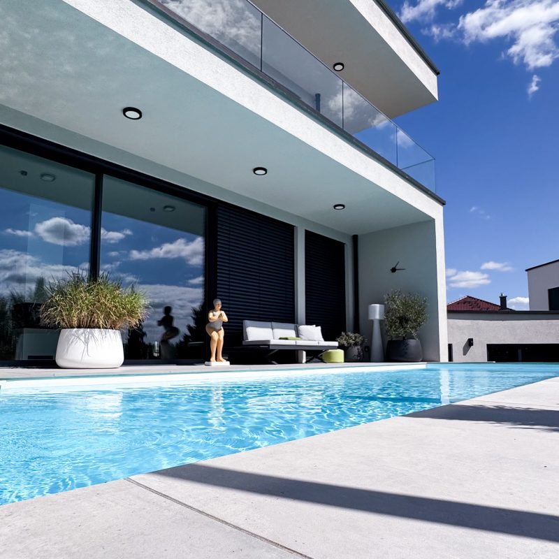 Moderne Rückansicht eines Einfamilienhauses mit Pool, überdachter Terrasse, Glasbalkon und großzügigen Fensterflächen.