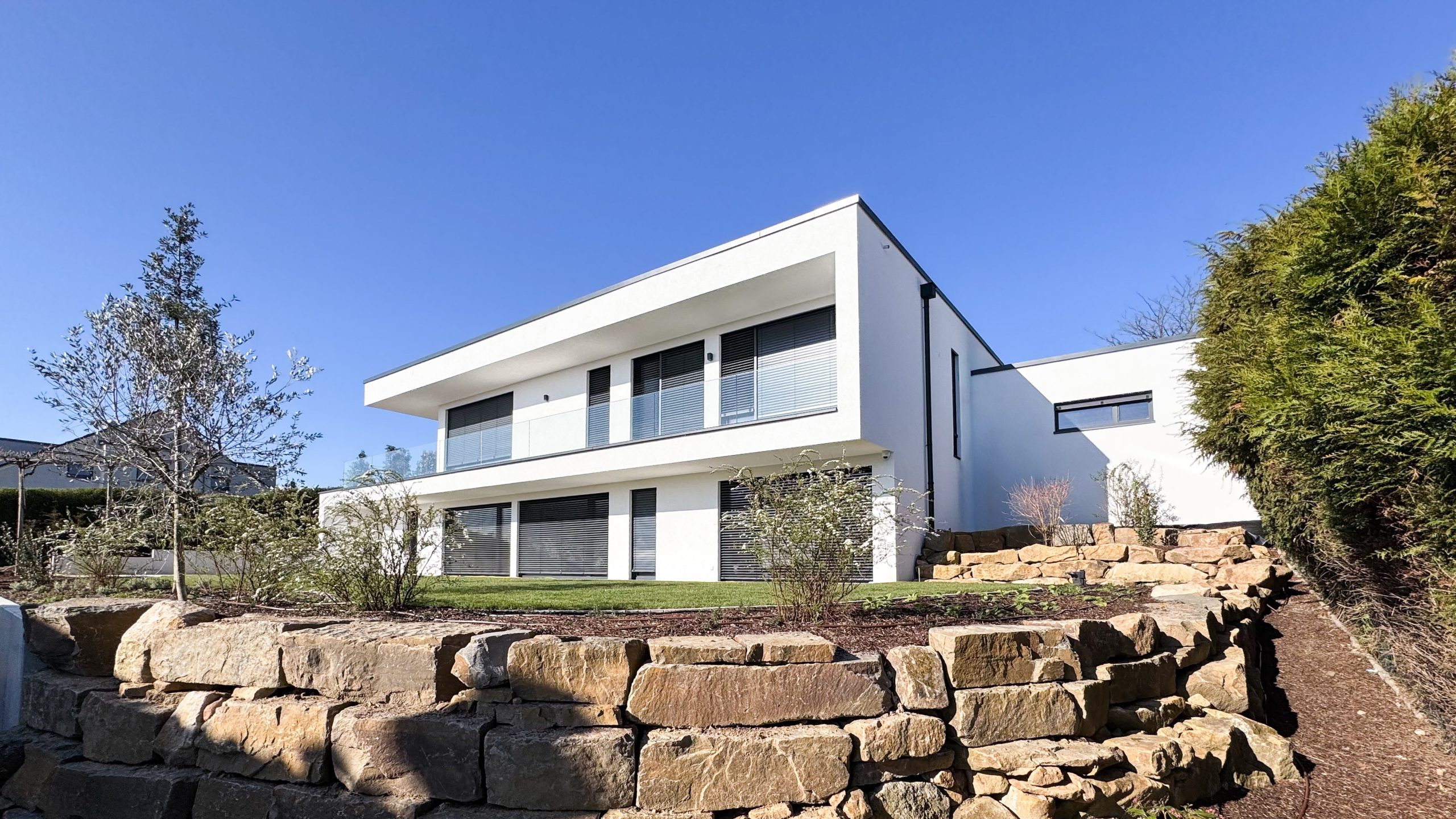 Moderne Rückansicht von #GERBERHAUS16 mit Natursteinmauer, Garten und klarer Architektur